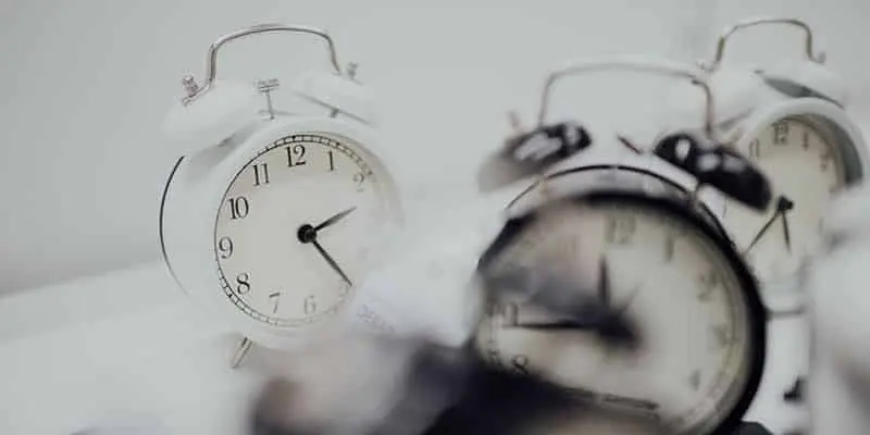 Multiple black and white old fashioned alarm clocks against a white background
