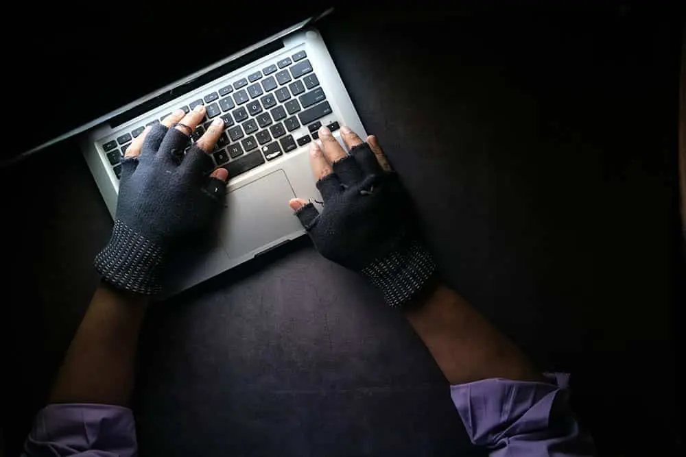 Arms of man wearing black fingerless gloves hovering over a laptop keyboard