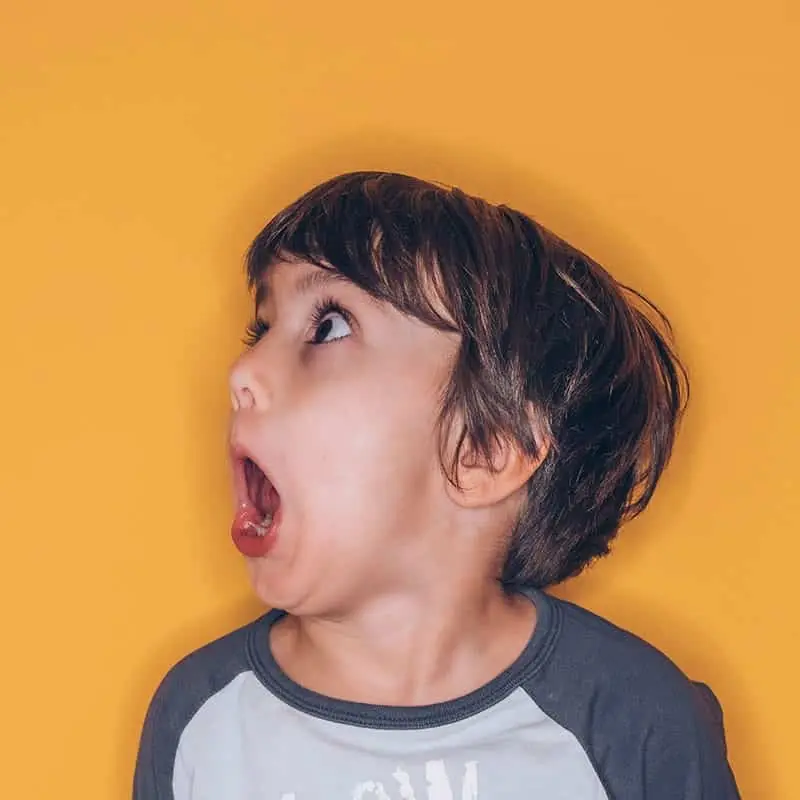 Young boy against a yellow background with a horrified look on his face