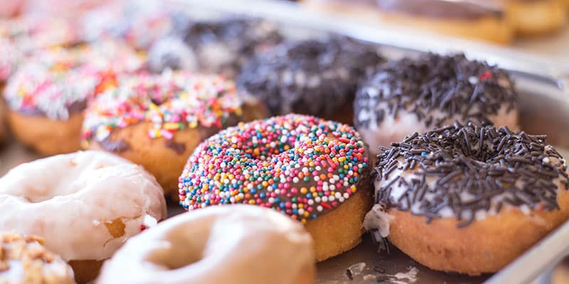 A tray of donuts with chocolate sprinkles, rainbow sprinkles and sugar glazed