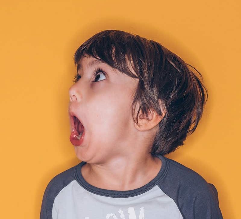 Young boy against a yellow background with a horrified look on his face