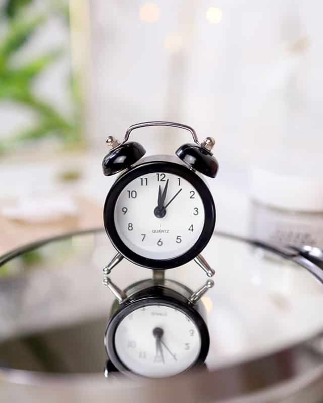 An old fashioned black and white alarm clock on a mirror
